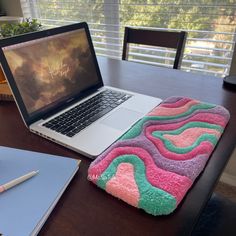 an open laptop computer sitting on top of a wooden desk next to a pink and green towel