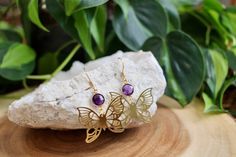 These beautiful dangle earrings feature 8mm gold plated hydro amethyst connectors and 25x33x brass butterfly charms. All connected to gold plated stainless steel earring hooks. Amethyst, known for its calming properties, brings a sense of tranquility. Paired with the butterfly, a symbol of transformation and rebirth, these earrings carry a meaningful message of personal growth and positive change. These earrings would be a thoughtful gift for someone with a February Birthday as amethyst is the b Handmade Gold Butterfly Earrings, Purple Brass Earrings As Gift, Gold Amethyst Earrings With Ear Wire, Gold Metal Earrings With Butterfly Charm, Gold Earrings With Butterfly Charm, Handmade Amethyst Gold Earrings, Handmade Gold Amethyst Earrings, Purple Butterfly Charm Earrings For Gift, February Birthstone Jewelry