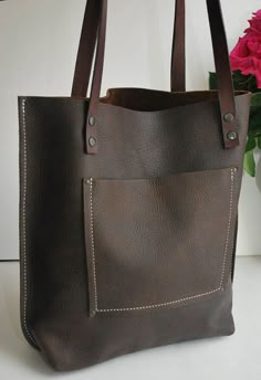 a brown leather tote bag sitting next to a pink flower