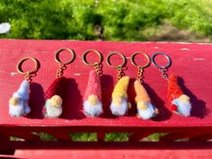 six keychains with different colored pom poms hanging from them on a red bench