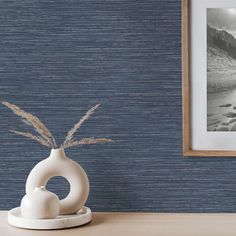 a white vase sitting on top of a wooden table next to a painting and framed photo