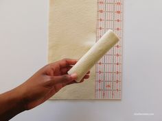 a person holding a piece of fabric next to a ruler on a wall with tape