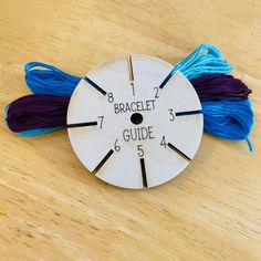 a white clock with blue and purple tassels on it's face sitting on a wooden table