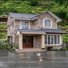 a stone house with a brown door and windows on the front, surrounded by green hills