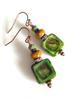 Gorgeous earthy green and mustard  Czech glass earrings featuring 14 mm table cut opaque green Czech squares with rustic Picasso finish. Copper Crystal rondelles, tiny olivine Czech glass beads and copper daisies are add accents.  Beautiful rich green Czech glass beads are wire wrapped on antique copper French hooks. Drop is 1 1/2 inch. Artisan Green Rectangular Jewelry, Green Rectangular Artisan Jewelry, Artisan Rectangular Green Jewelry, Green Bohemian Rectangular Earrings, Green Rectangular Bohemian Earrings, Czech Glass Bead Earrings, Handmade Square Green Earrings, Handmade Green Square Earrings, Square Green Handmade Earrings