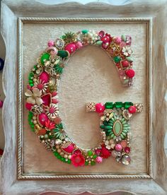 the letter o is made out of beads and flowers in a frame on top of a table