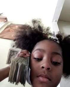 a woman holding money in front of her face and looking at the camera with an afro