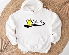 a white hoodie with the word softball on it next to a straw hat and palm tree