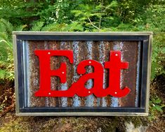 a metal sign with the word eat painted on it in front of some trees and bushes