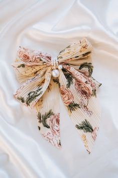 A bow for those who like to stand out! Our Find Me Bow features a unique floral print in pleated fabric with pearl center details, all on a classic french barrette. Add some pizzazz to any outfit--you won't be able to stay hidden with this head-turner! Approx. 6.5" x 9.5" Fabric bow French barrett clip Bows And Ribbons, Pale White Skin, Bow Designs, French Barrette, Fabric Bows, Pleated Fabric, Contemporary Outfits, Makeup Bags, Bow Design