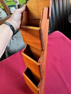 a person holding an open wooden drawer on top of a pink cloth covered tablecloth