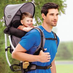 a man carrying a child in a baby carrier on his back with trees in the background