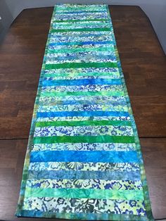 a long table runner made with blue, green and white fabric on top of a wooden floor