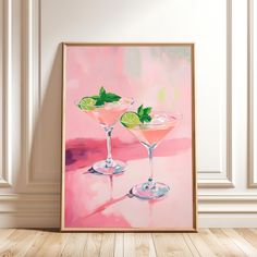 two martinis with lime slices on the rim in front of a pink background