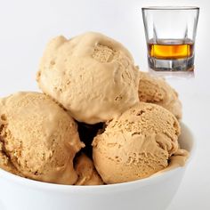 three scoops of ice cream in a white bowl next to a glass of whiskey