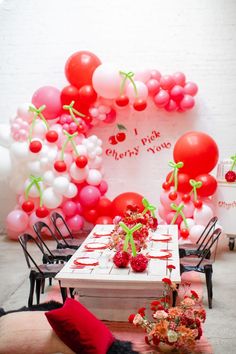 the table is set up for a party with red and white balloons, cherries, and other decorations