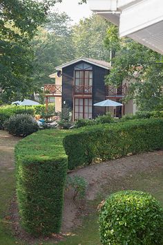 the house is surrounded by lush green bushes and trees with umbrellas in the yard