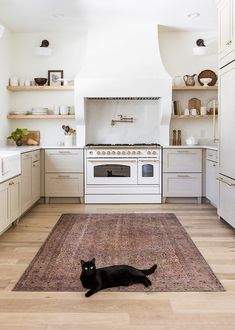 a black cat laying on the floor in a kitchen with white cabinets and an oven