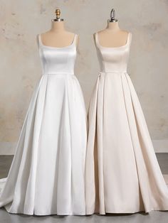 two white dresses on mannequins in front of a wall