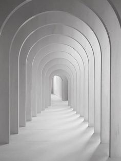 an empty hallway with white walls and arches leading into the light at the end in black and white