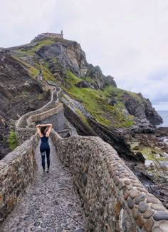 a woman walking down a stone path next to the ocean with her hands on her head