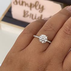 a woman's hand with a diamond ring on top of her finger and a box in the background