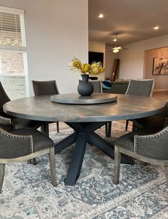 a dining room table with four chairs and a vase on top of it in front of a window