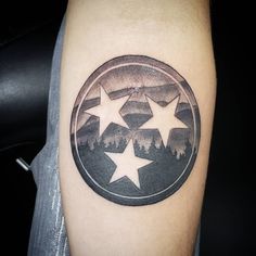 a black and white photo of a star tattoo on the right arm with trees in the background