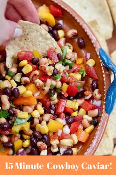 a hand dipping a tortilla chip into a bowl filled with beans and corn