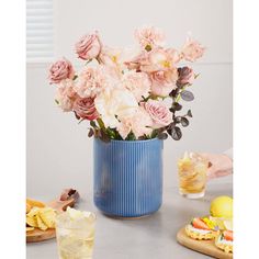 a blue vase filled with pink flowers sitting on top of a table next to drinks