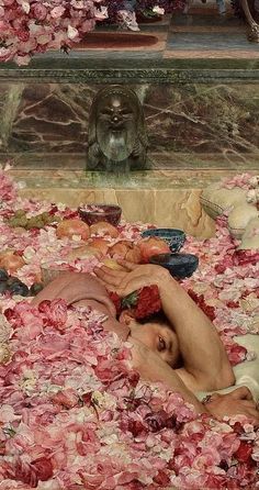 two people laying on the ground surrounded by pink flowers and other things in front of a statue