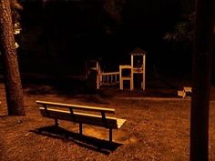 a park bench sitting in the middle of a grass field at night with playgrounds and trees