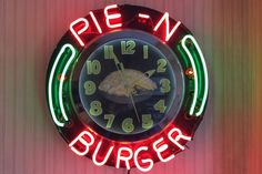 a neon sign that says pie n burger on the side of a wall with a clock