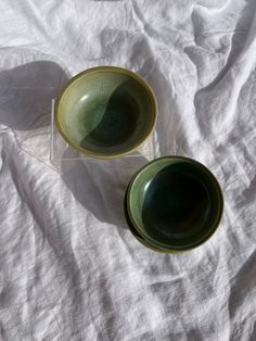 two green bowls sitting on top of a white cloth covered tablecloth next to each other