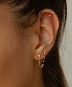 a close up of a woman's ear wearing gold chain and pearled earrings