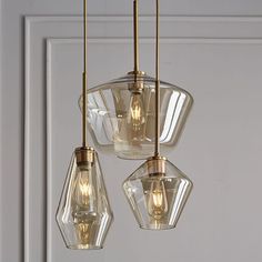 three clear glass pendant lights hanging from a white door with gold trim and brass fittings