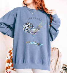 Celebrate your love for skiing and après ski festivities with this chic and playful sweatshirt! Featuring a stylish martini glass with crossed skis and a disco ball, this design embodies the fun and relaxation of après ski moments. Perfect for ski enthusiasts and cocktail lovers alike, this sweatshirt will keep you warm and stylish whether you're lounging by the fire after a day on the slopes or heading to a winter party. Crafted from soft, cozy fabric, this sweatshirt is ideal for layering during ski season or for casual winter wear. How To Order 1. Please, check and review all photos. 2. Select your Sweatshirt size and color. 3. Click add to cart. Continue shopping for free shipping! ($35 minimum) 4. If finished, Click "Proceed to check out" to finalize.  5. Carefully review all items as Casual Graphic Print Tops For Winter Sports, Casual Skiing Tops, Crew Neck Tops For Ski Season, Casual Winter Skiing Tops, Long Sleeve Ski Tops For Ski Season, Long Sleeve Skiing Tops For Ski Season, Long Sleeve Tops For Ski Season And Winter Sports, Casual Graphic Print Top For Skiing, Long Sleeve Tops For Ski Season