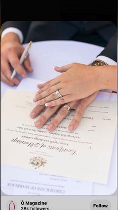 two people sitting at a table with wedding rings on their hands and papers in front of them