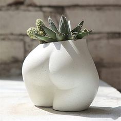 a white vase sitting on top of a table next to a brick wall with succulents in it