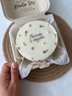 someone is holding up a cake in a box with writing on the side and flowers all over it