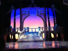 the stage is lit up with purple and blue lights on it's sides as people sit at benches in front of an archway