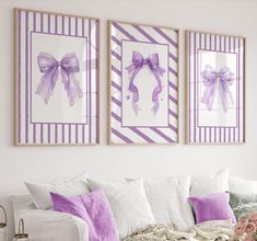 three framed pictures hang on the wall above a white couch with purple and white pillows