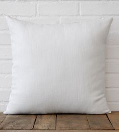 a white pillow sitting on top of a wooden table next to a brick wall and floor