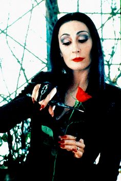 a woman with long black hair and red lipstick holding a rose in her right hand