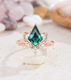 a ring with an emerald colored stone surrounded by white stones and other jewelry on a table