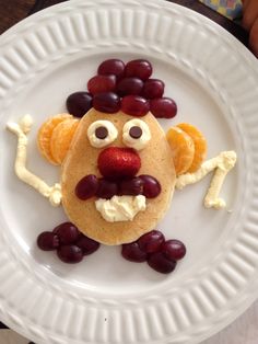 a white plate topped with pancakes covered in fruit and cheese, as if it were a face