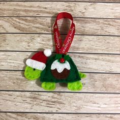 a christmas ornament with a green turtle wearing a santa hat and holding a red ribbon