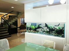 a fish tank in the middle of a dining room table with chairs and a staircase behind it