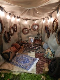 a bed covered in lots of pillows and blankets with lights strung from the ceiling above it