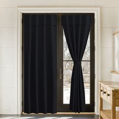 black curtains hanging on the side of a door in a room with white walls and flooring